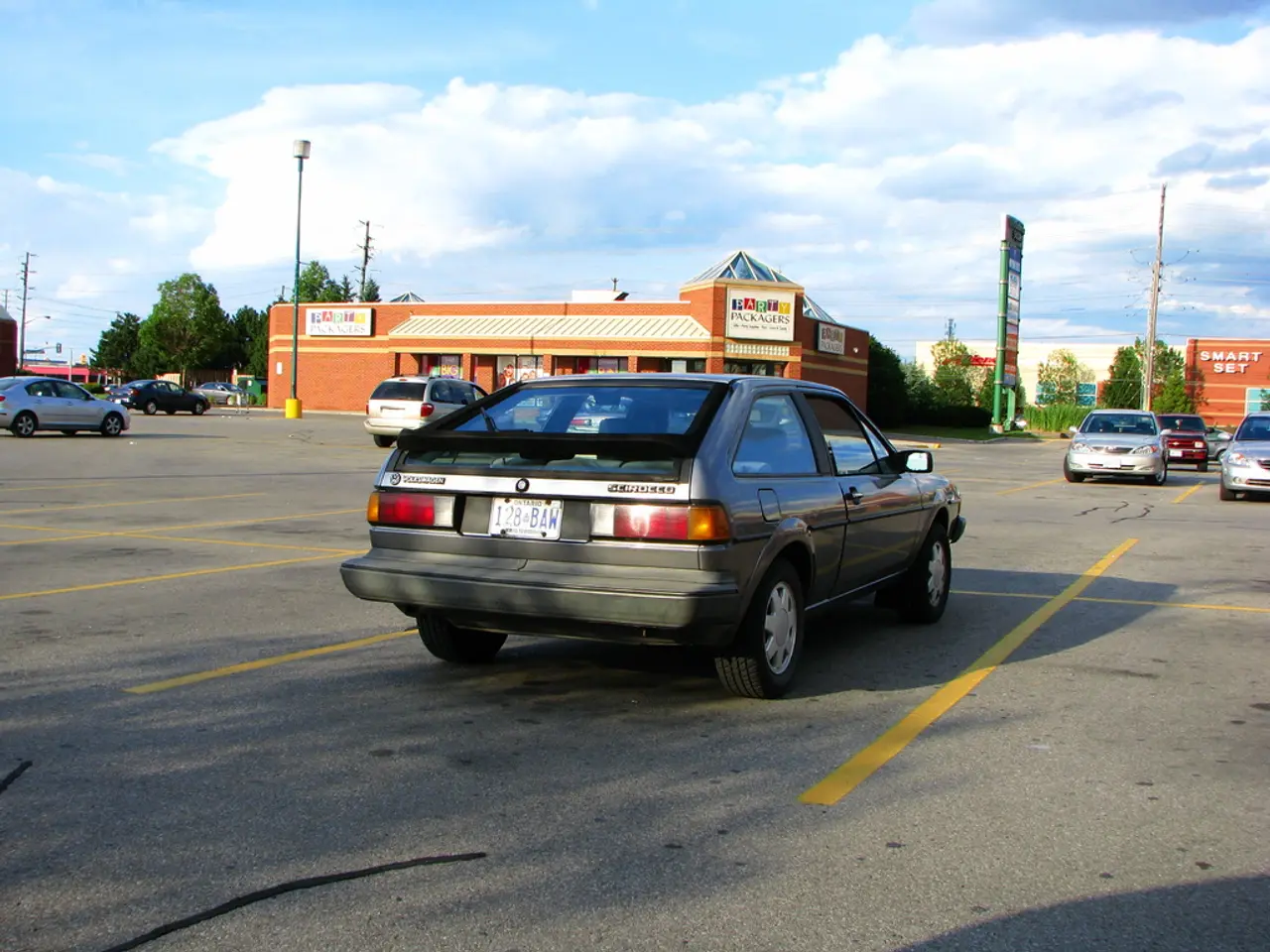 In this image there are cars on a road, in the background there are poles, buildings, trees and the...