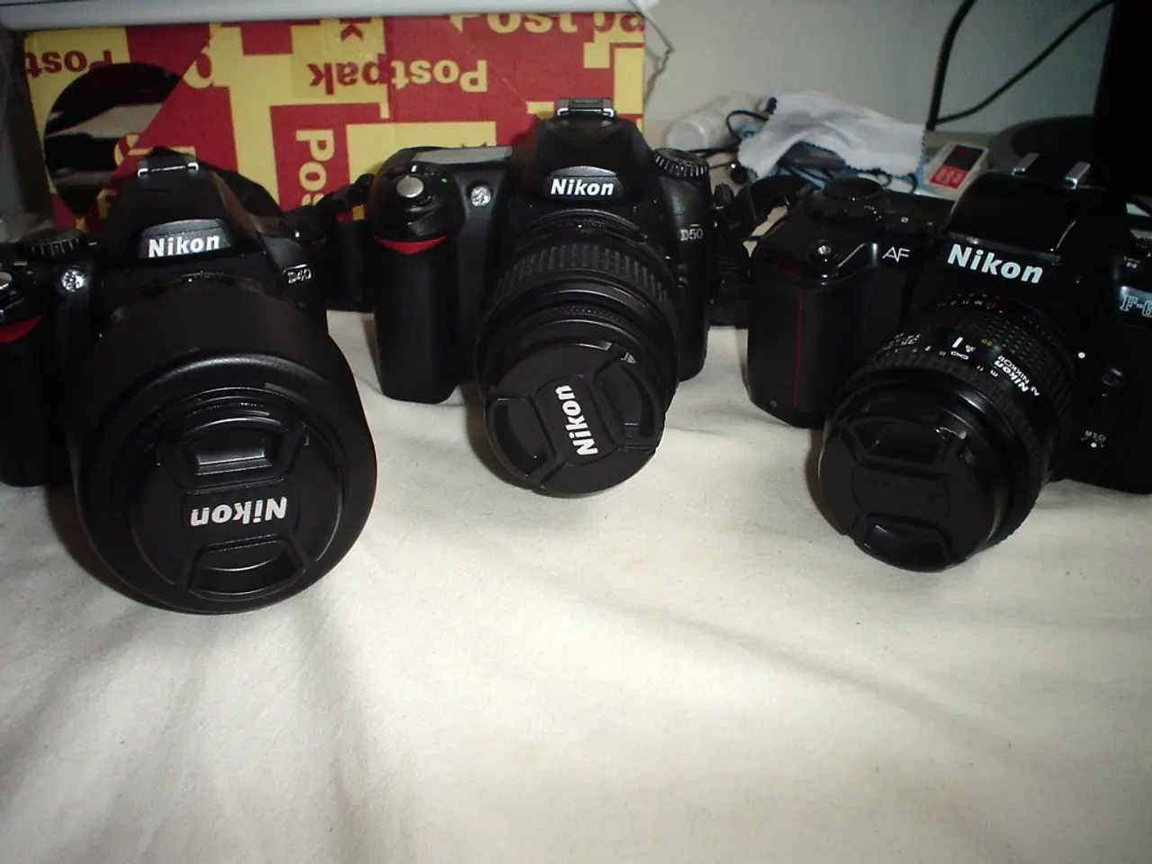 In this image I can see three cameras which are black in color on the white colored cloth. In the...