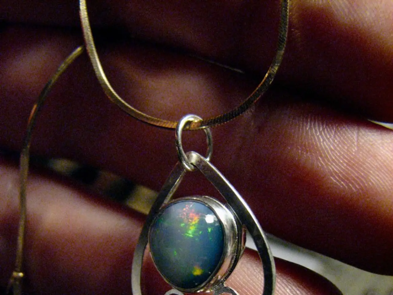 In this picture I can see a chain with a pendant, there are fingers of a person.