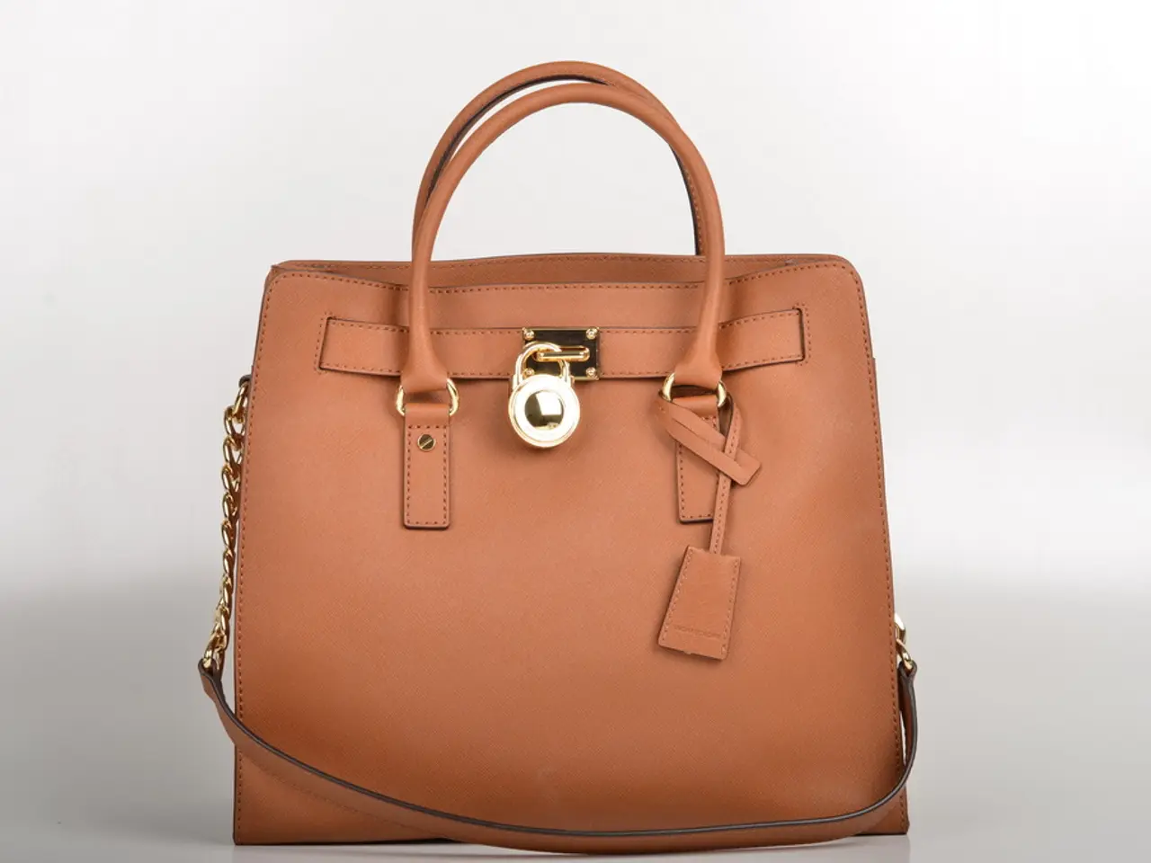 In this image there is a bag of brown colour having a lock in the middle and chain at the left...