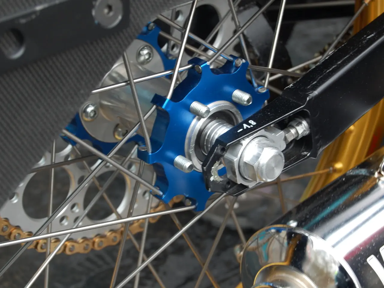 In this image we can see there is a motorbike wheel and a silencer.