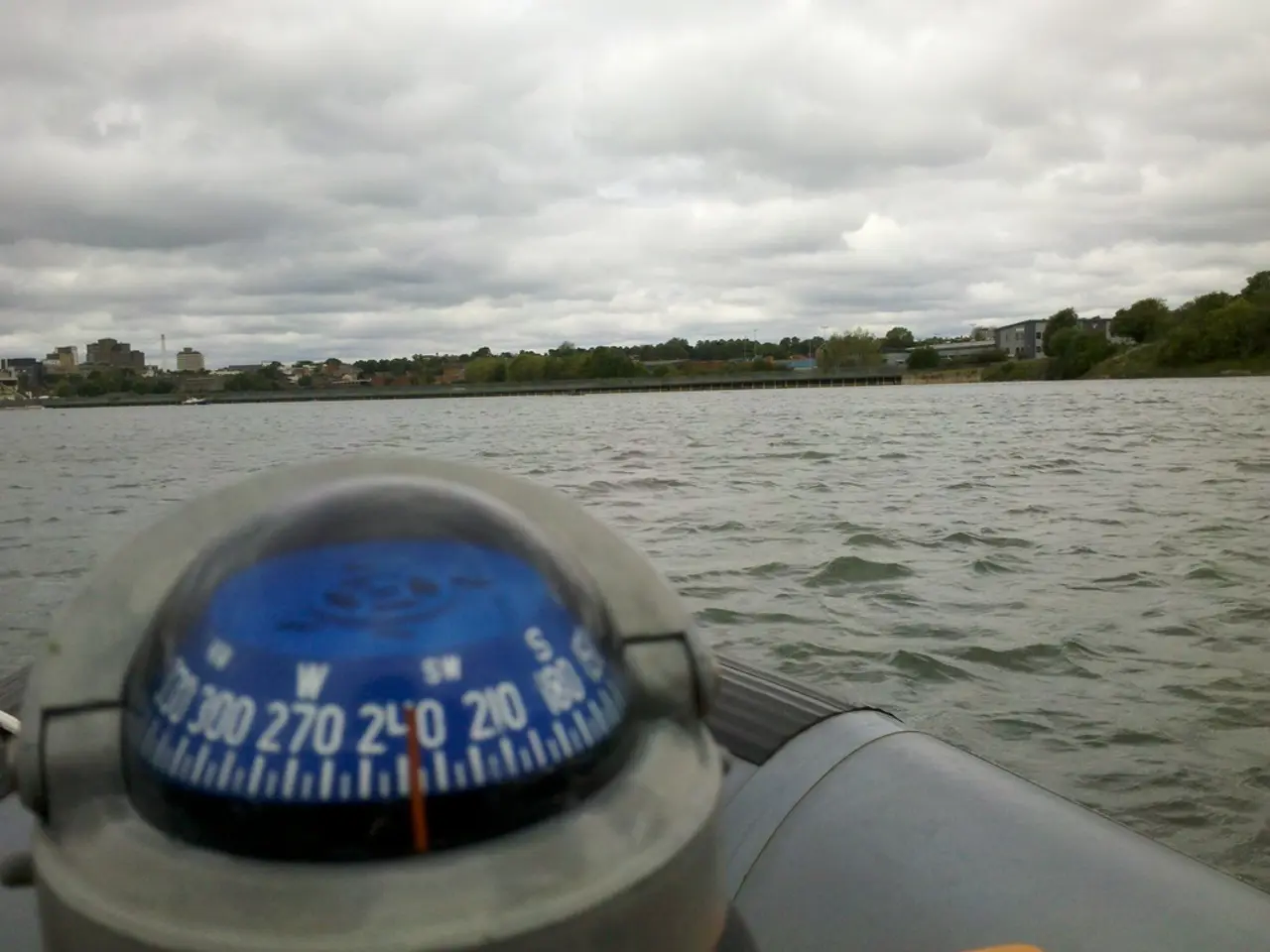 In this image in the foreground we see a compass and in the middle there is a water and background...