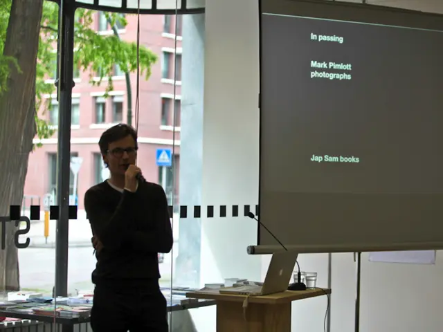 It is an office there is a person standing and speaking through a mic to his right side there is a...