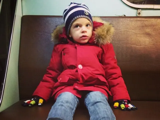 As we can see in the image there is a girl wearing red color jacket and sitting on sofa.