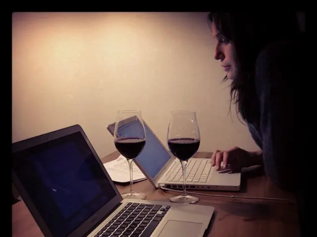 In the picture there is a woman who is working with the laptop, there are two laptops, two glasses,...