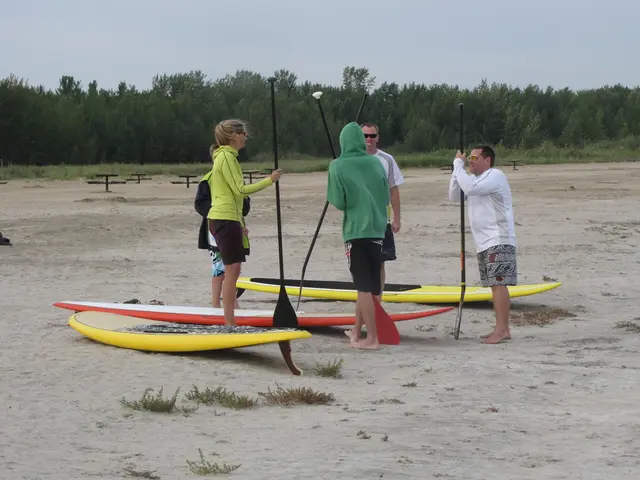 In this image there are surfboards on the ground. Near to them there are five people standing. They...