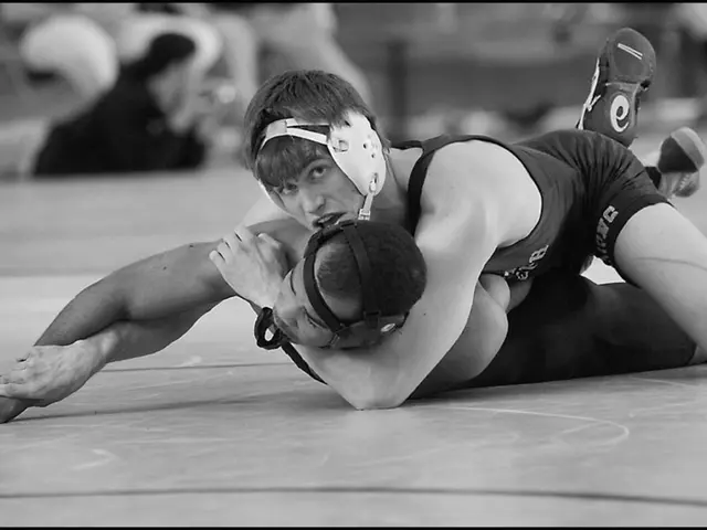 In the center of the image there are two persons wrestling on the ground. In the background there...