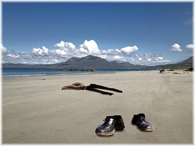 In this image there are shoes and clothes on the surface of the sand, in the background of the...