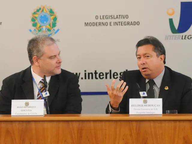 In this image I see 2 men who are wearing suits and I see a table in front of them on which there...