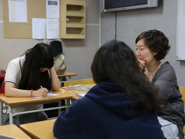 These 3 women are sitting on a chair. Posters on wall. A white board and television on wall. We can...